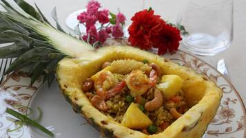 Eine Schüssel mit Garnelen-Reis-Gericht in einer Ananas-Schale, mit Blumen und einem Glas Wasser auf dem Tisch.