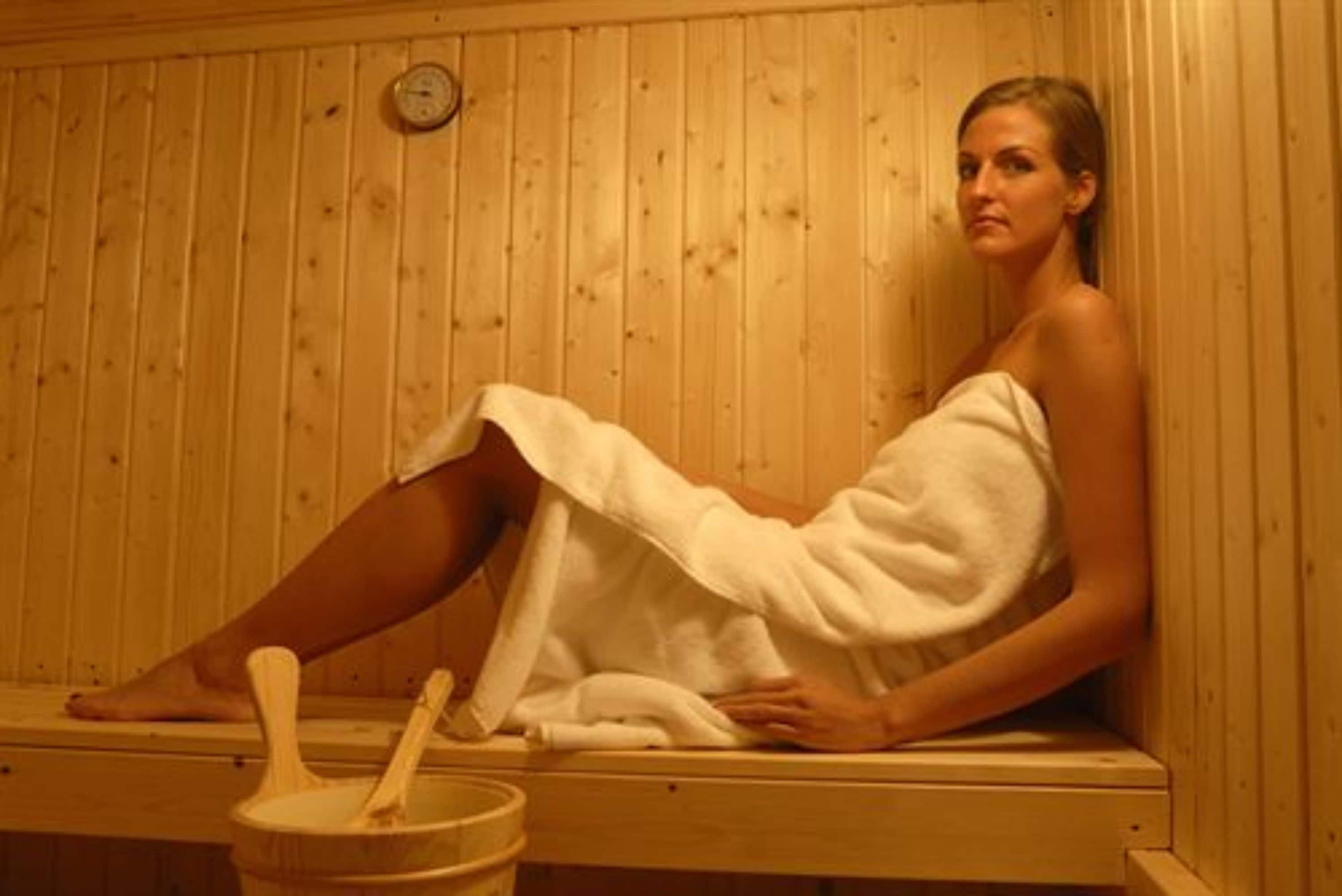 A person in a wooden sauna with a wooden bench and a wooden bucket.