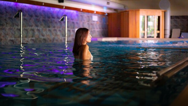 A person in a swimming pool with a stone wall and wooden paneling in the background. - Cocca Hotel Royal Thai SPA (Sarnico)
