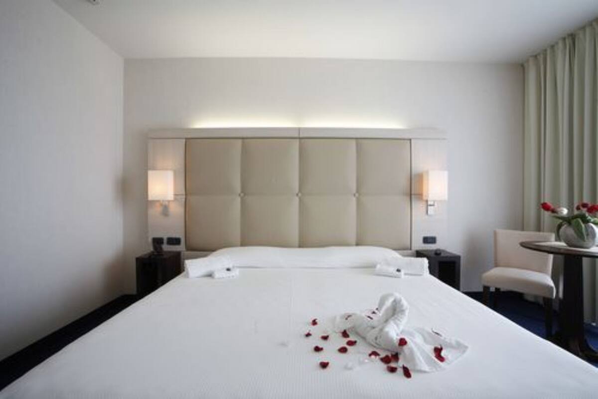 Ein Hotelzimmer mit einem großen Bett, zwei Nachttischlampen, einem kleinen Tisch mit Blumenvase und einem Sessel.