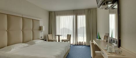 Una habitación de hotel con una cama grande, un escritorio con silla, una mesita y un televisor montado en la pared.