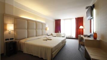 A hotel room with a large bed, a desk, a TV, and a window with curtains.