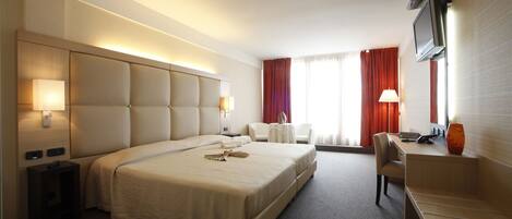 A hotel room with a large bed, a desk, a TV, and a window with curtains.