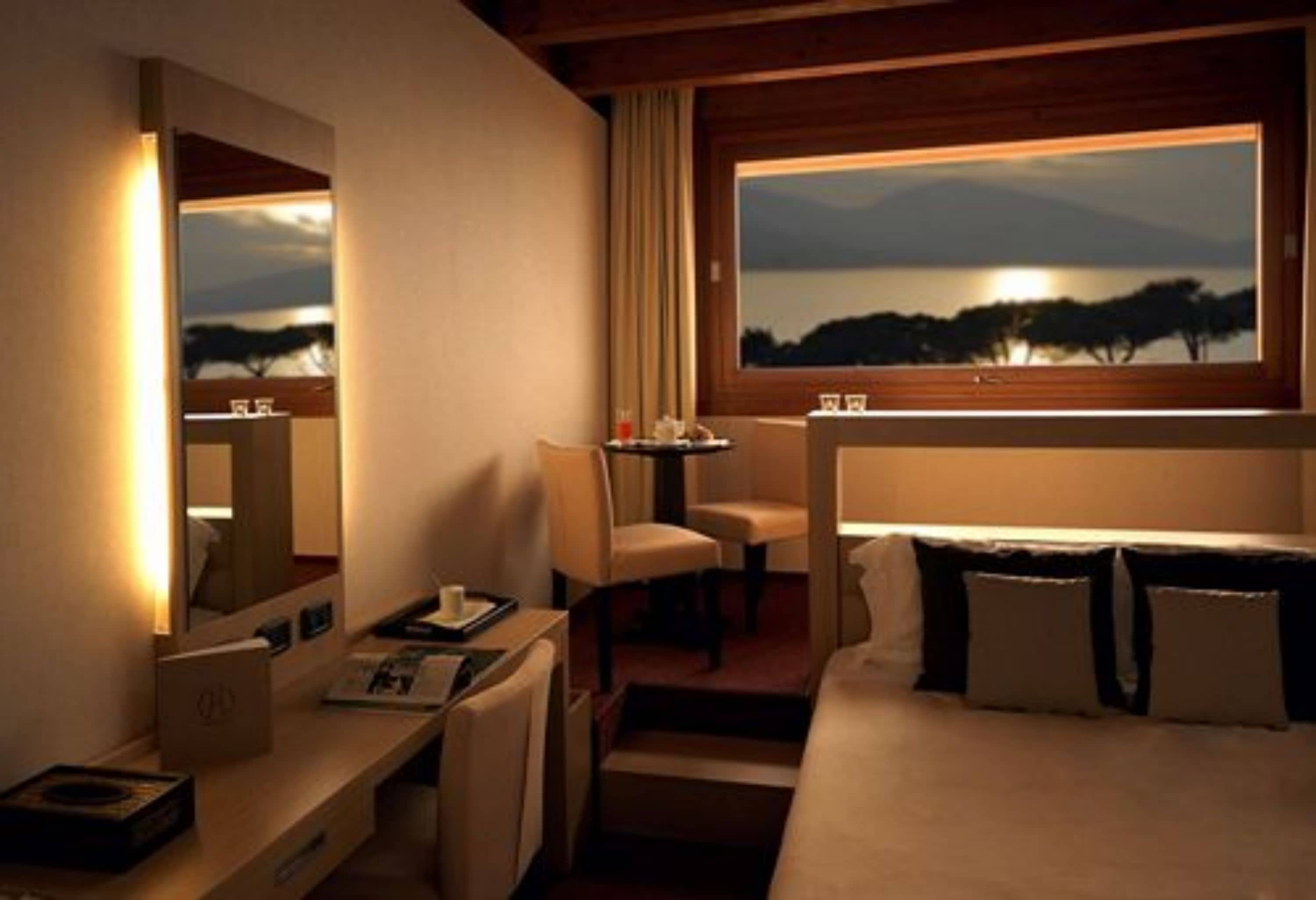 Habitación de hotel con cama, escritorio, silla, ventana con vista al lago y espejo.