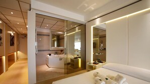 A modern hotel room with a large bed, a glass-enclosed shower area, a vanity with a mirror, and a bedside table with a phone and a lamp. - Cocca Hotel Royal Thai SPA (Sarnico)