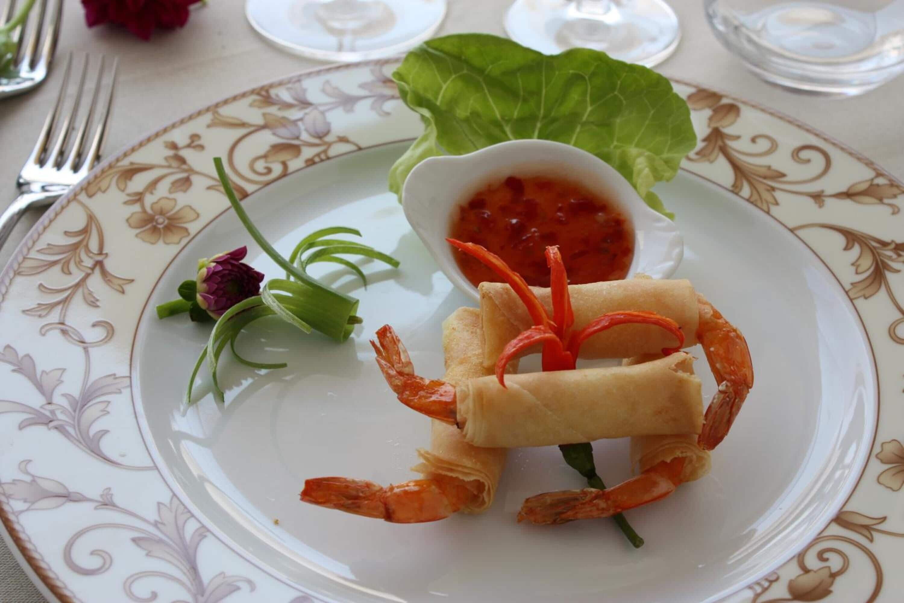 Ein Teller mit einem gerollten Frühlingsrollen, Garnelen und einer kleinen Sauce.