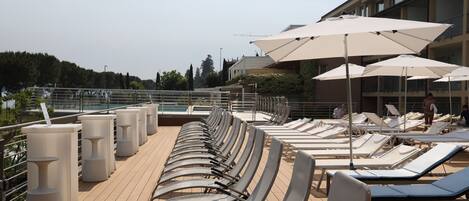 Terraza con sillones de descanso y sombrillas, con vistas a una piscina y un edificio con balcones.