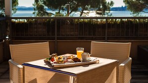 A balcony with wicker chairs, a table with breakfast, and a view of the water and trees. - Cocca Hotel Royal Thai SPA (Sarnico)
