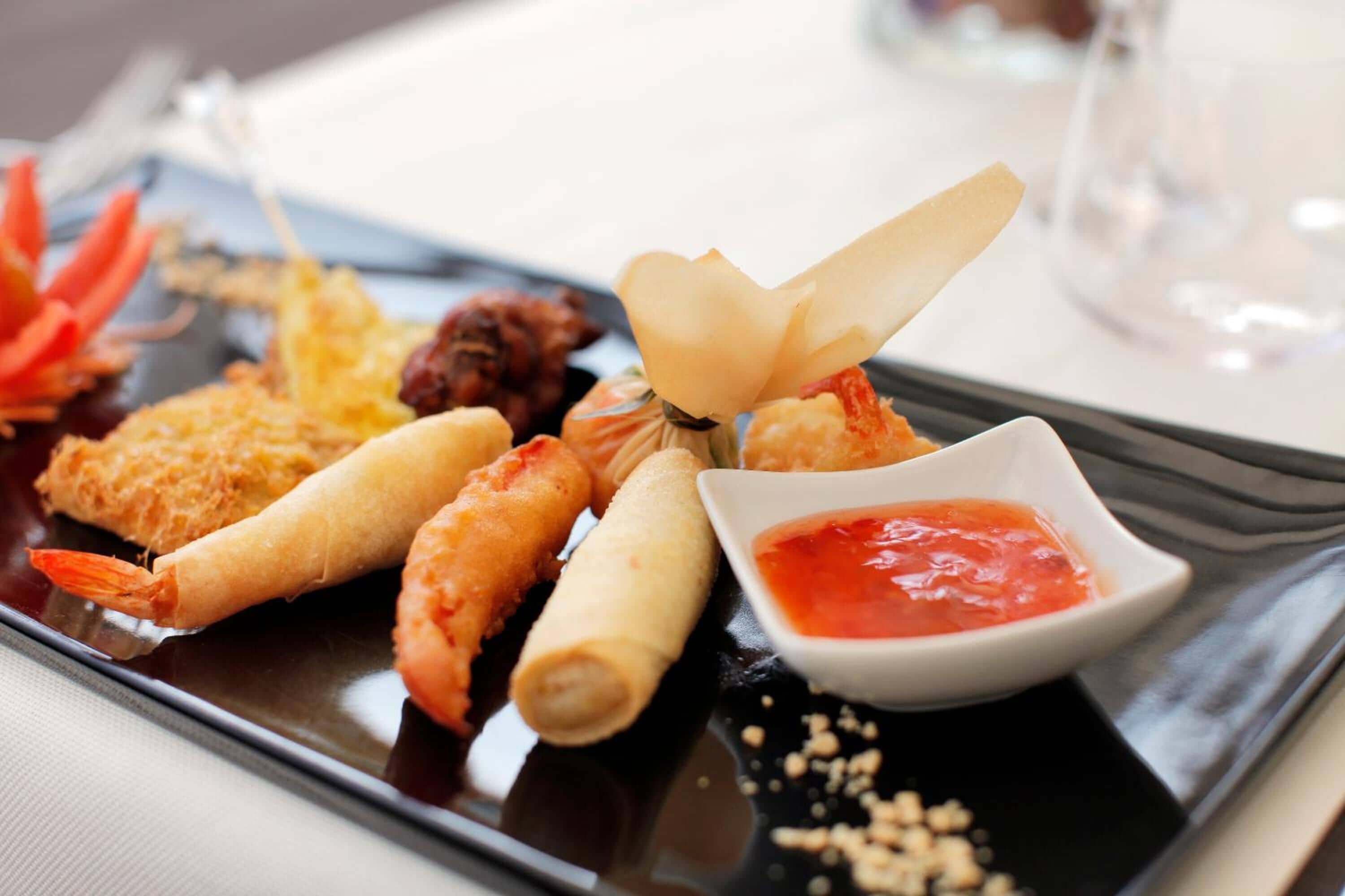 A tray of assorted seafood appetizers, including shrimp and rolls, with a small bowl of dipping sauce.