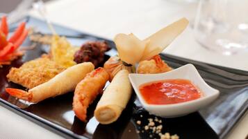 A tray of assorted seafood appetizers, including shrimp and rolls, with a small bowl of dipping sauce.