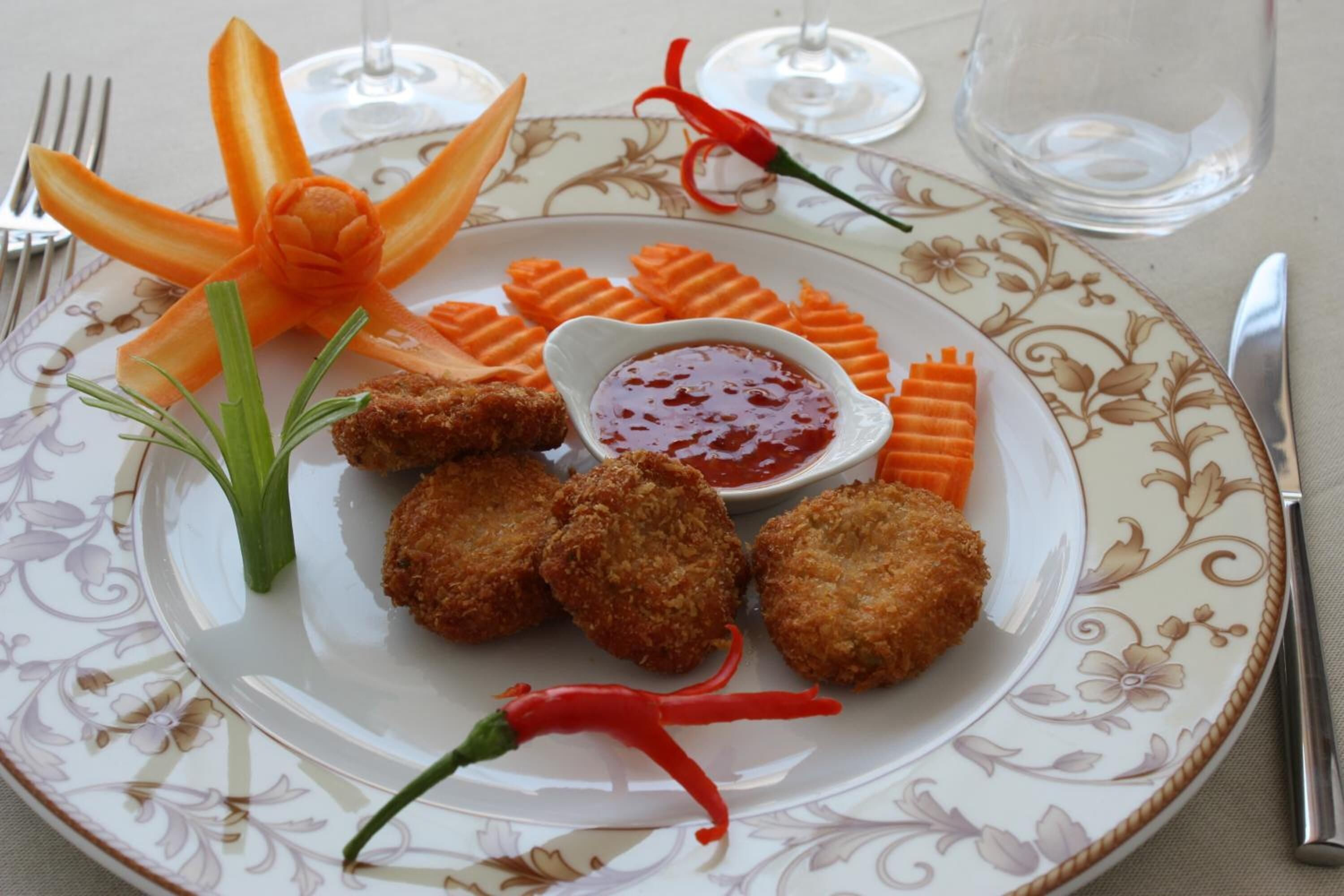 Un plato con alimentos rebozados, zanahorias y un recipiente pequeño con salsa, todo dispuesto sobre una bandeja decorativa.