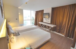Ein modernes Hotelzimmer mit zwei Betten, einem Schreibtisch, einem Fernseher und großen Fenstern mit Vorhängen.