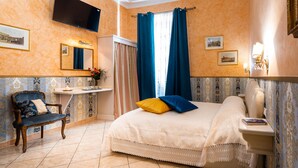 Quarto de hotel com uma cama, uma mesa de vaidade com espelho, uma cadeira e uma televisão fixada na parede.