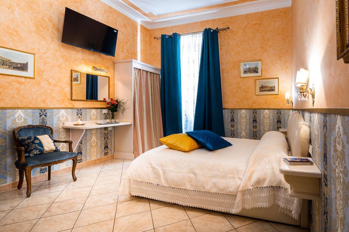A hotel room with a bed, a vanity with a mirror, a chair, and a television mounted on the wall.