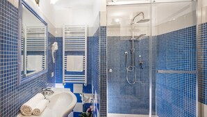 Uma casa de banho com chuveiro em cabine de vidro, um lavatório branco com espelho e paredes com azulejos azuis.