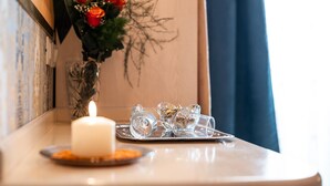 Uma mesa com uma vela branca, um vaso de vidro com flores vermelhas e laranja, e uma bandeja com copos de cristal.