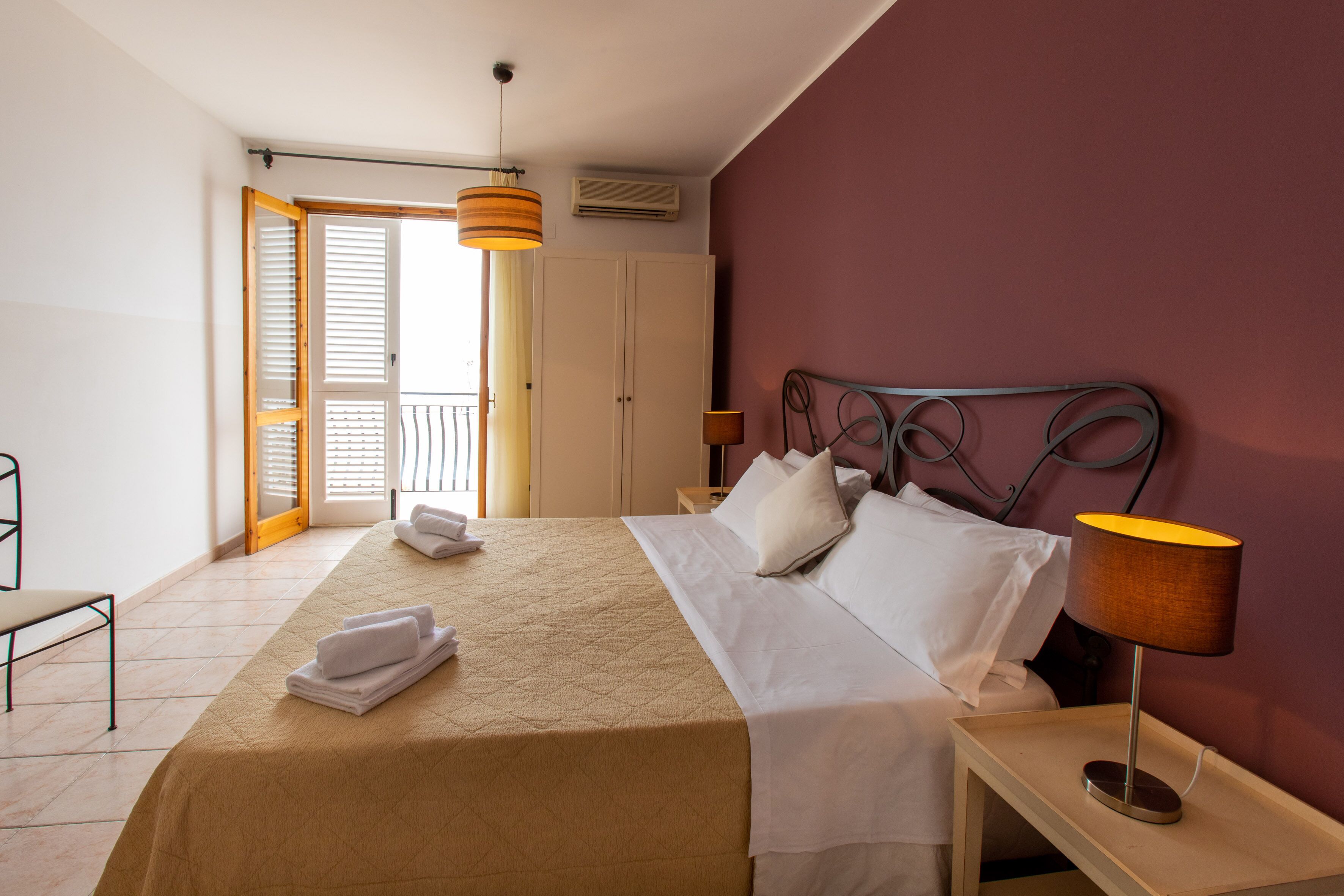 Una habitación de hotel con una cama, una mesita de noche, una lámpara y una puerta que da a un balcón.