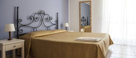 Une chambre à coucher avec un lit, deux tables de chevet, un miroir et une fenêtre avec des rideaux.
