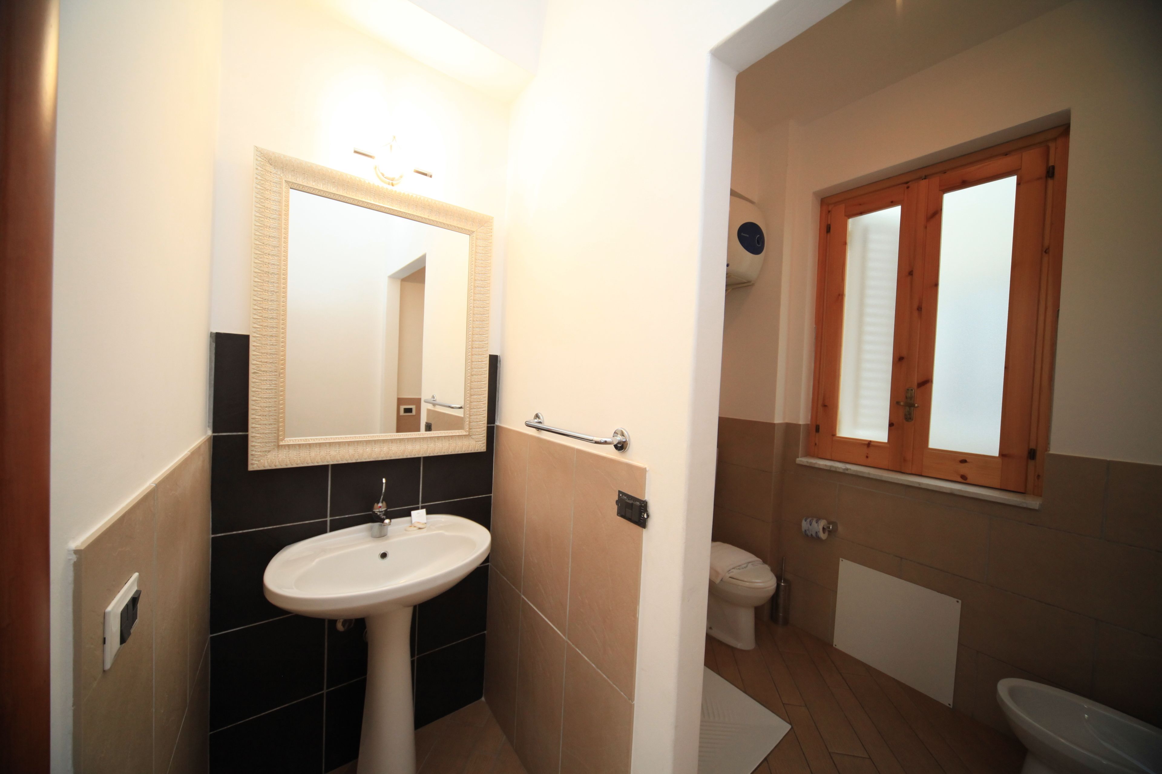 A bathroom with a white sink, a mirror, a toilet, and a window.
