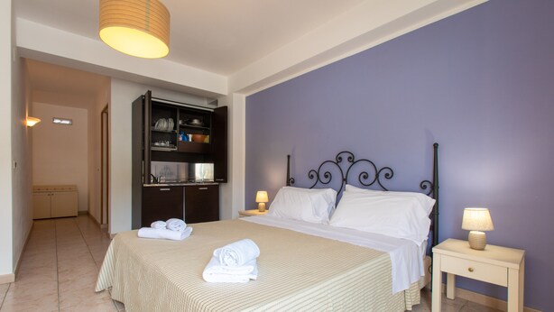 Een slaapkamer met een bed, nachtkastjes, een garderobe en een badkamer in de achtergrond.
