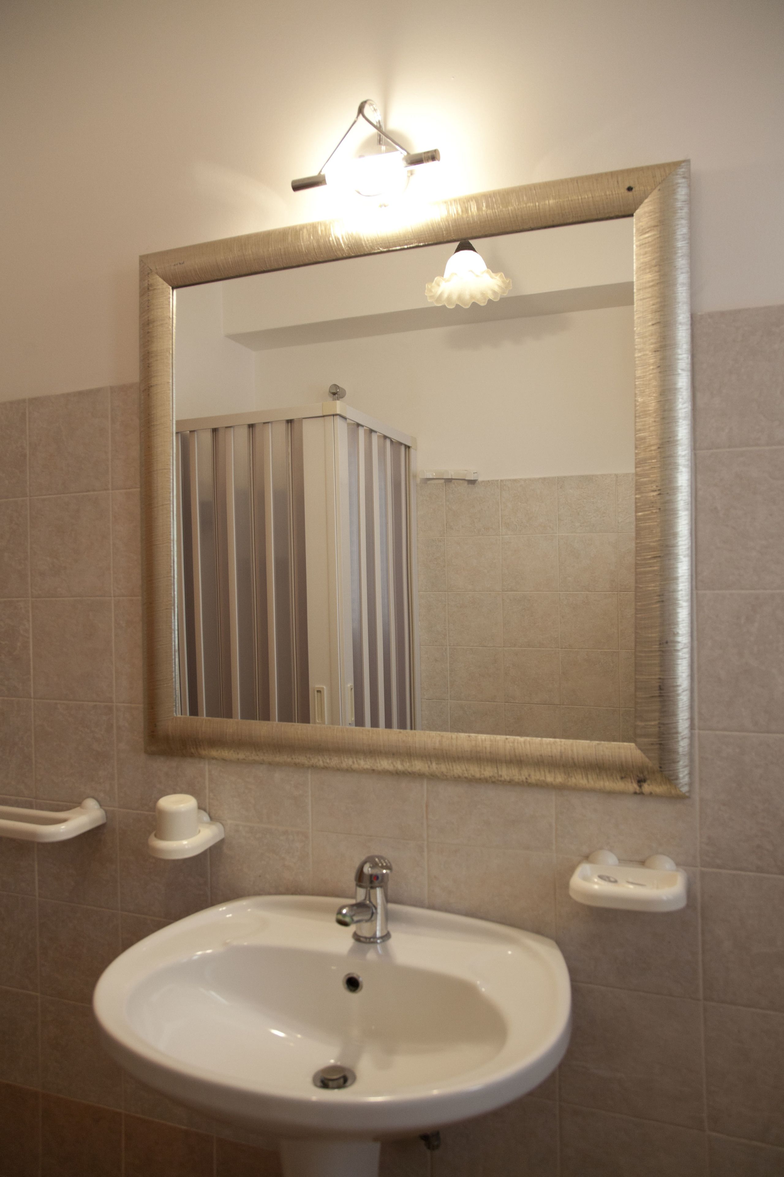 Une salle de bain avec un lavabo blanc, un miroir doté d’un cadre doré et un luminaire placé au-dessus du miroir.
