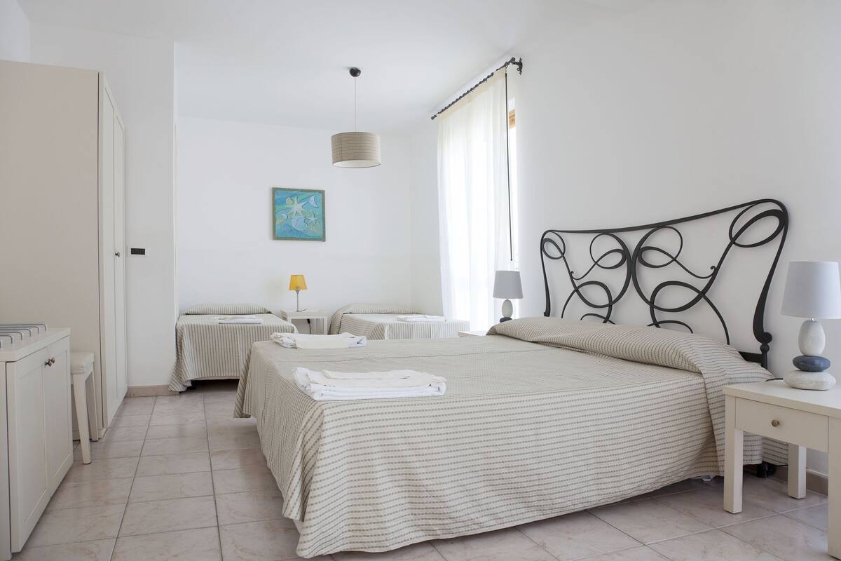 Un dormitorio con una cama grande, mesitas de noche, un armario y una ventana con cortinas.