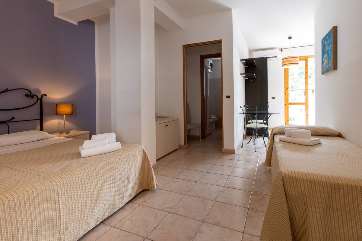 Habitación de hotel con dos camas, un escritorio, una silla y un baño visible a través de una puerta abierta.