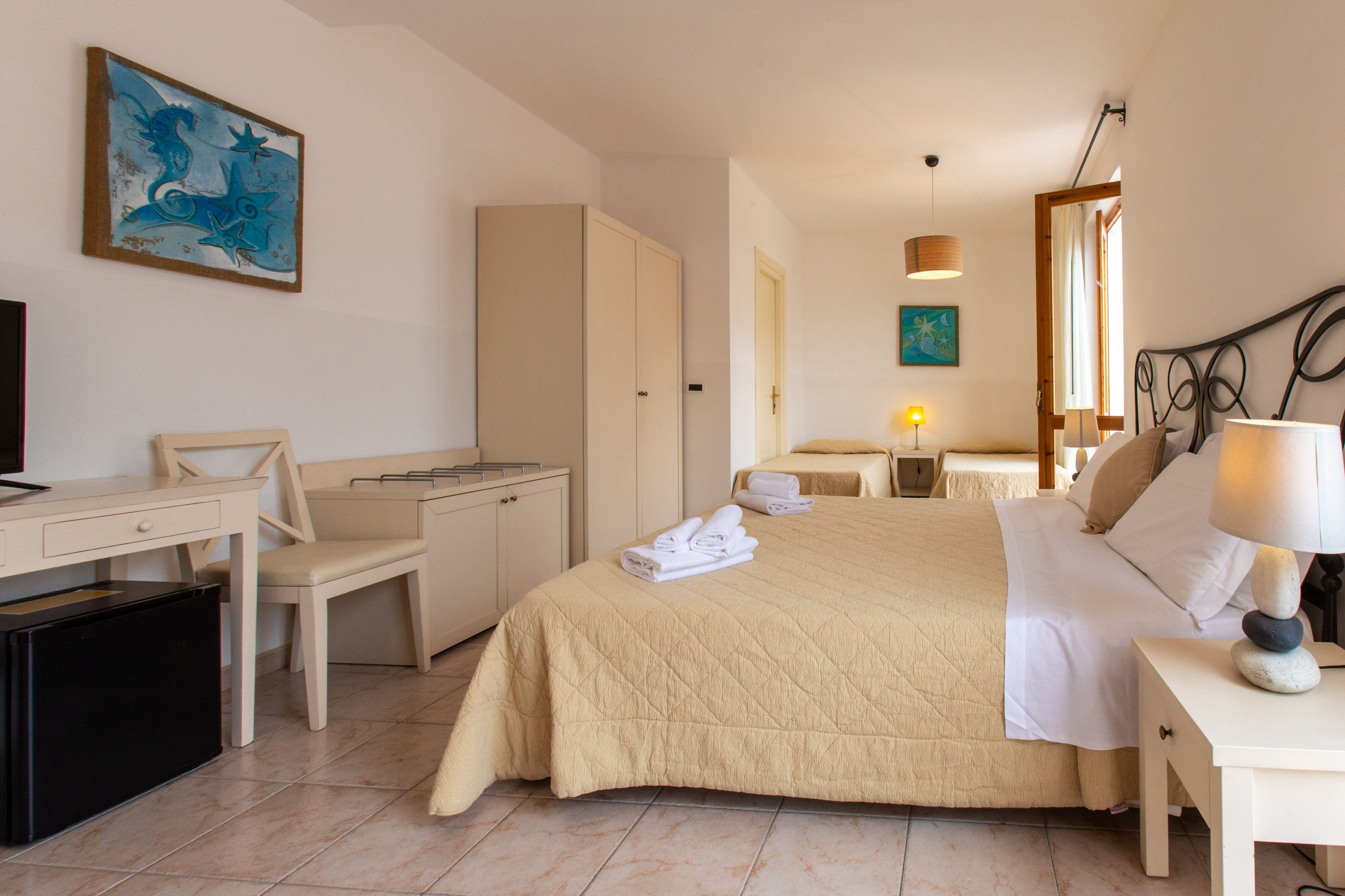 A hotel room with a bed, desk, chair, wardrobe, and a small table with a lamp.
