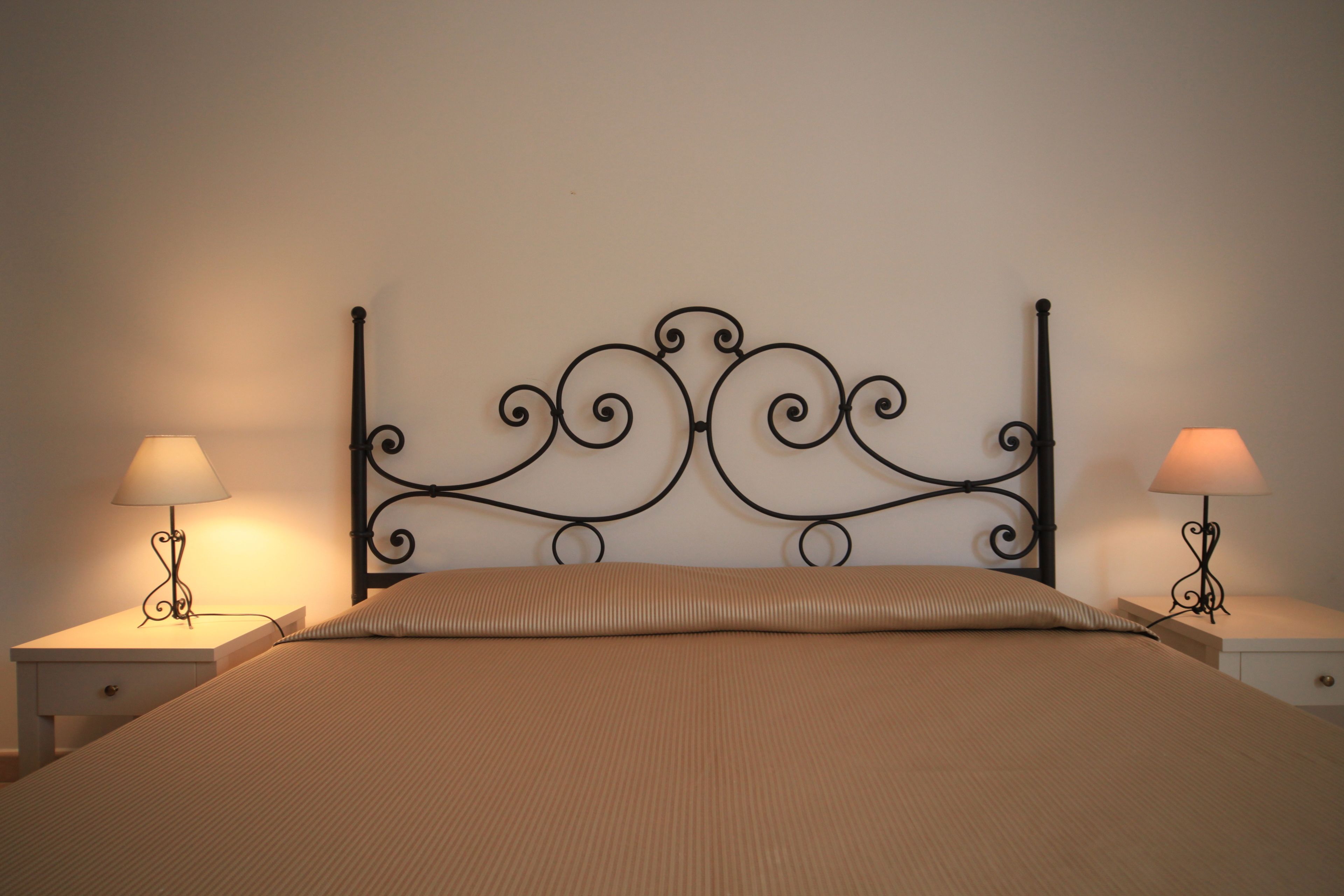 Een bed met een metalen hoofdbord, twee nachtkastjes met lampen en een effen muur.