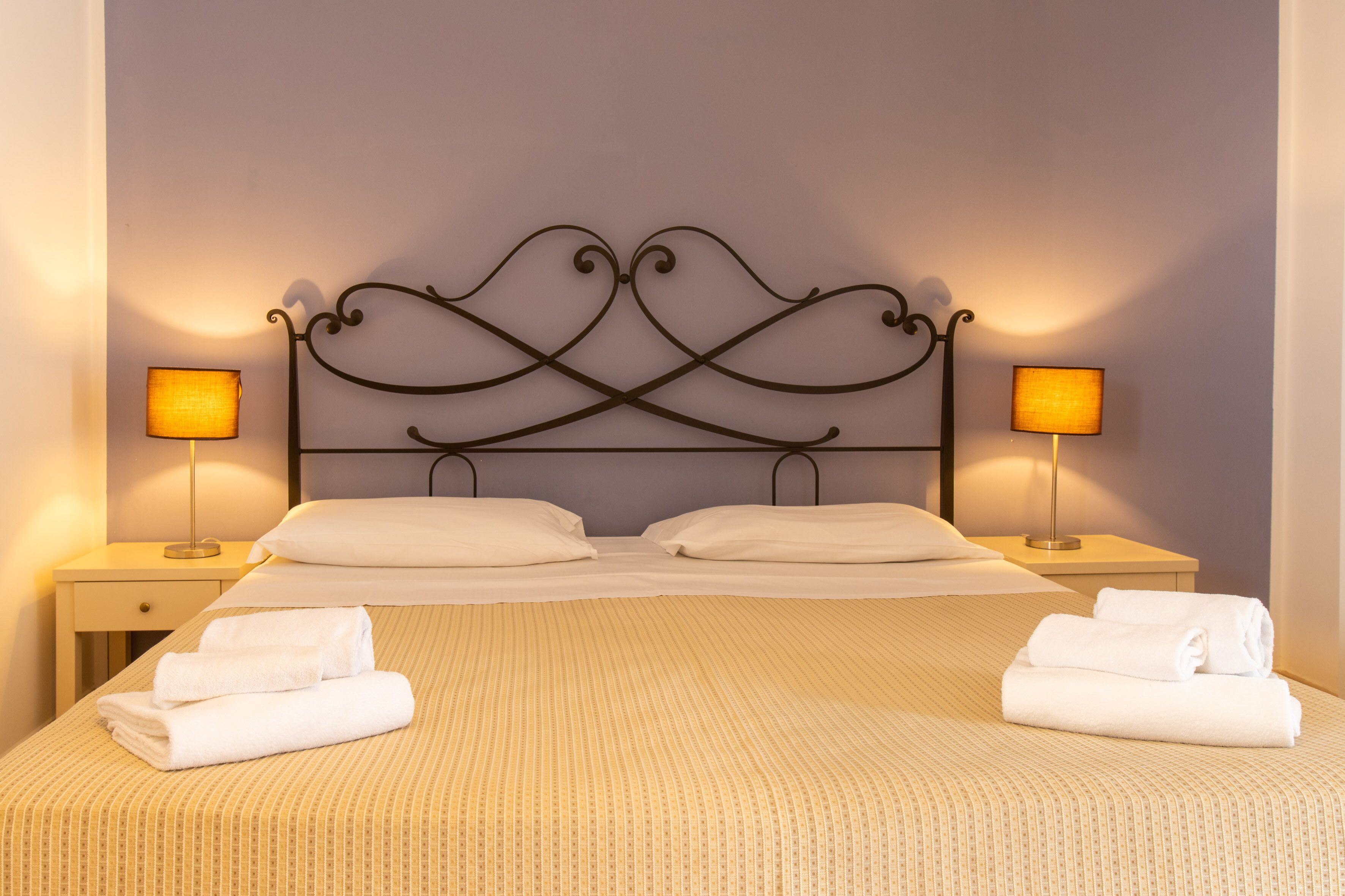 A neatly made bed with a patterned bedspread, two bedside lamps, and two folded towels on the nightstands.