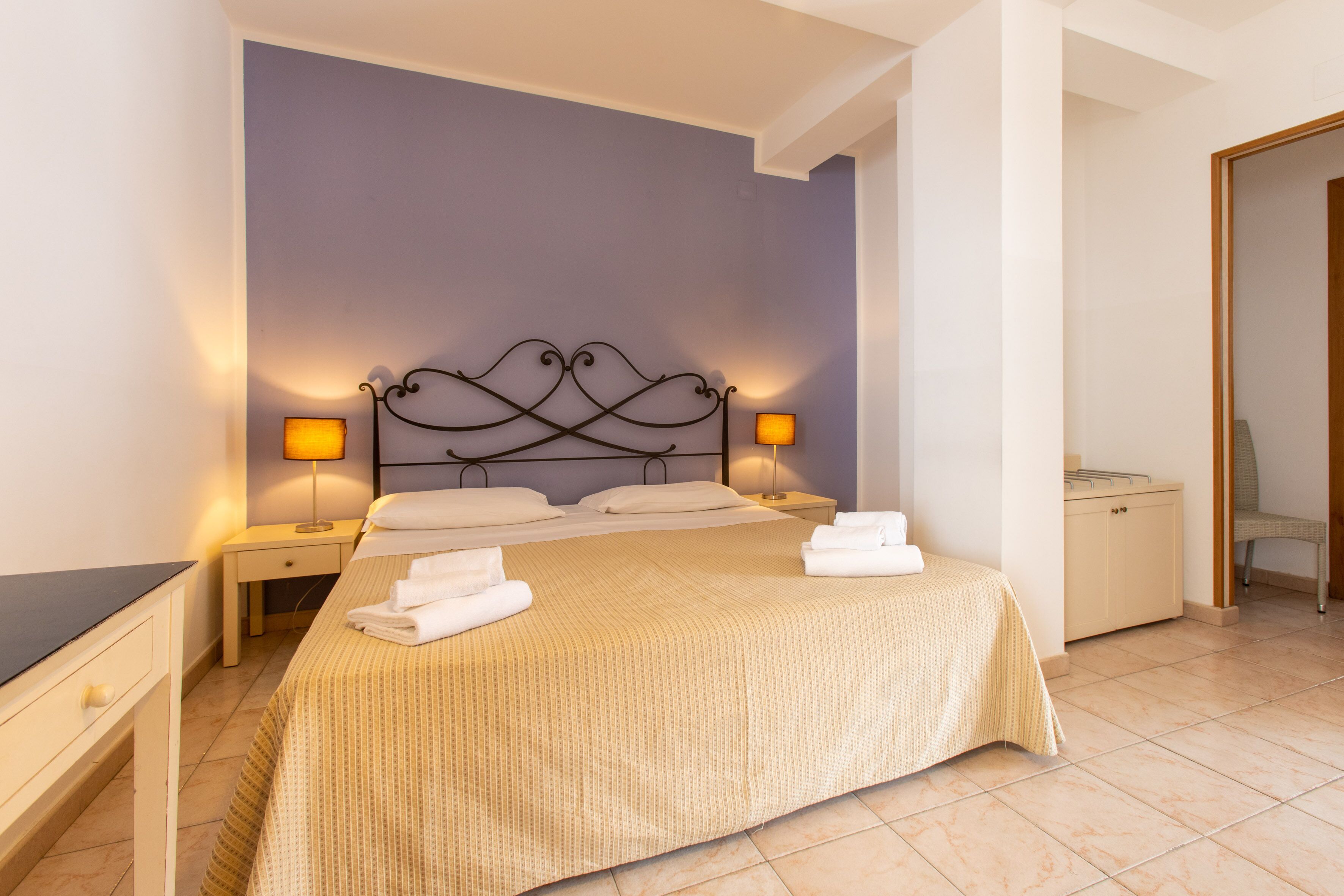 A neatly made bed with a beige bedspread, two bedside lamps, and a nightstand with a lamp.