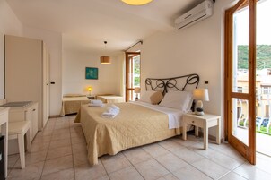 A hotel room with two beds, a desk, a chair, a lamp, and a window with a view of buildings.