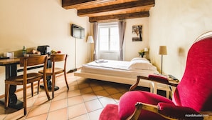 A hotel room with a wooden ceiling, a bed, a desk with chairs, a TV, and a window with curtains.