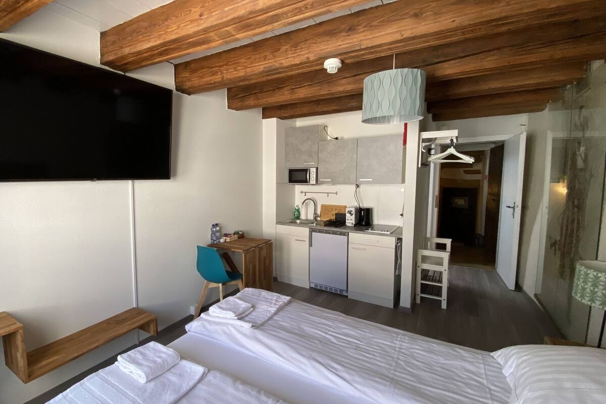 Un dormitorio con cama, escritorio, silla, televisión, kitchenette y baño.