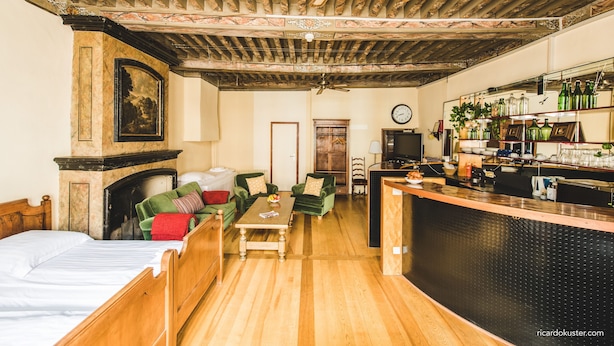 A room with a bed, a sofa, a coffee table, a fireplace, a television, and a bar area with bottles and glasses.