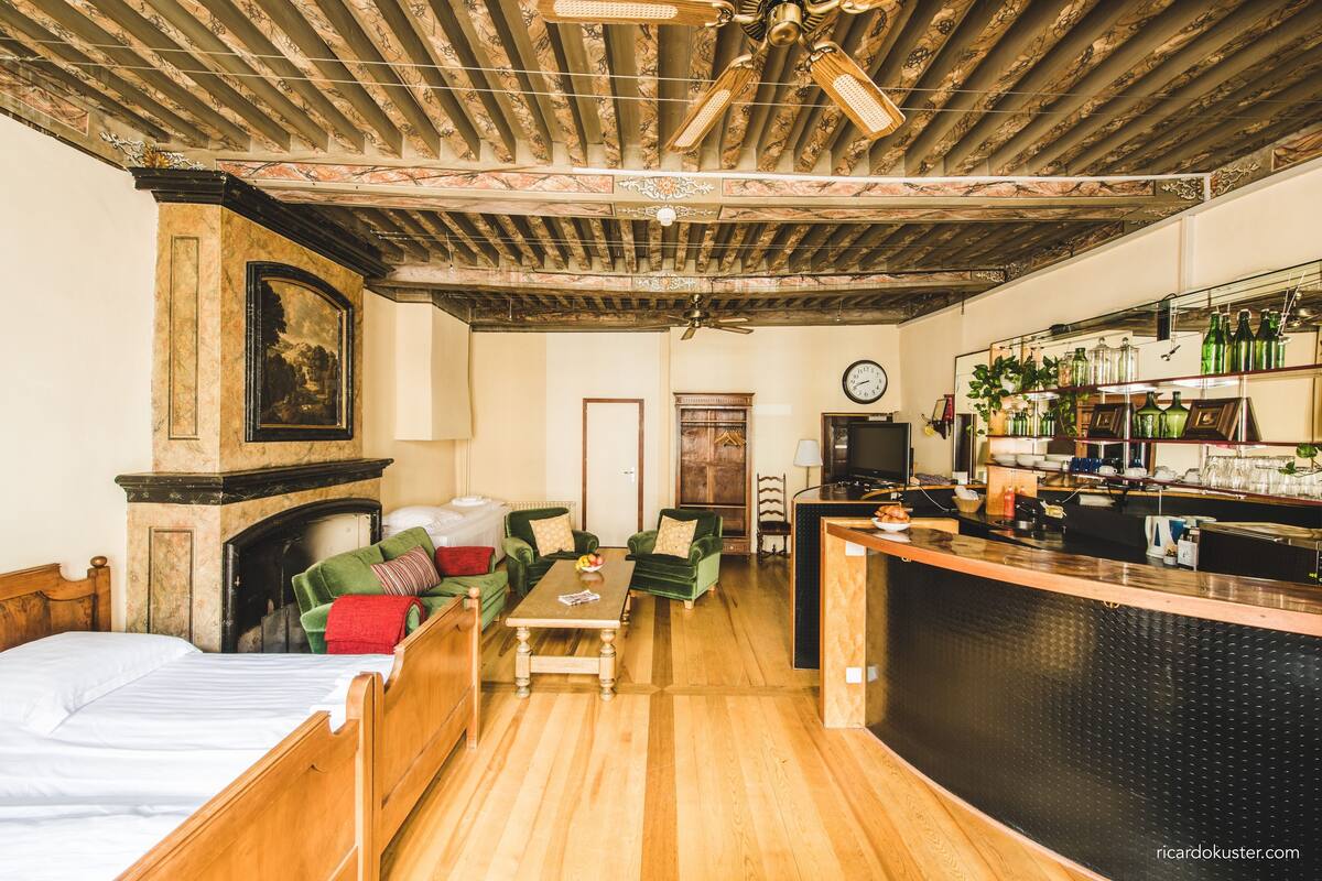Una habitación con cama, sofá, mesa de centro, chimenea, televisor y zona de bar con botellas y vasos.