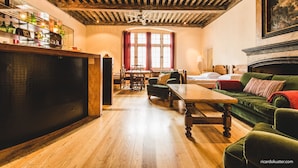 A room with a wooden ceiling, a fireplace, a green sofa, a wooden table, and a window with red curtains.