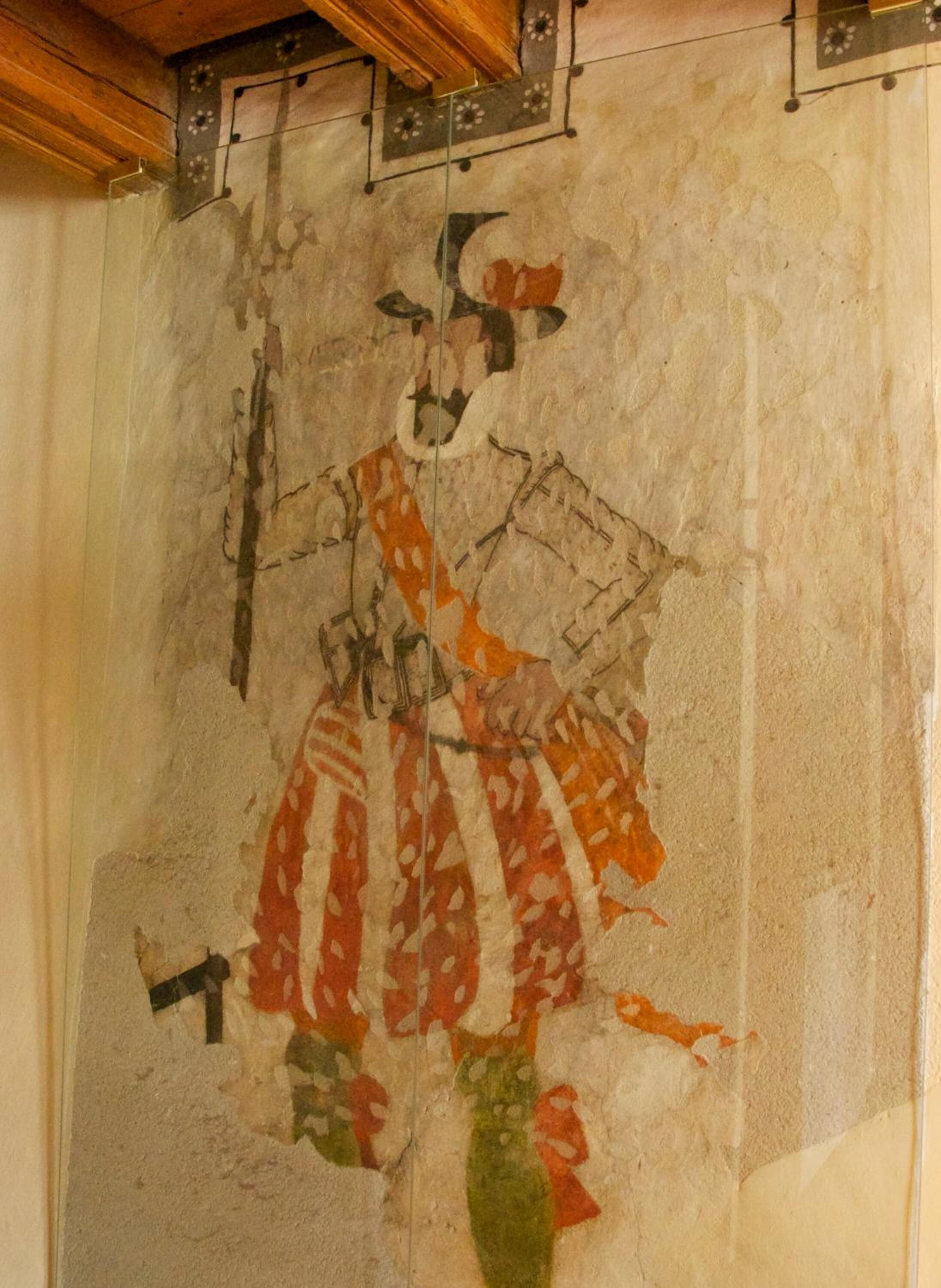 Un muro con un affresco sbiadito raffigurante una figura che regge un ventaglio.