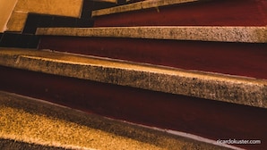 A spiral staircase with stone steps and a handrail, leading to a landing with two small windows.