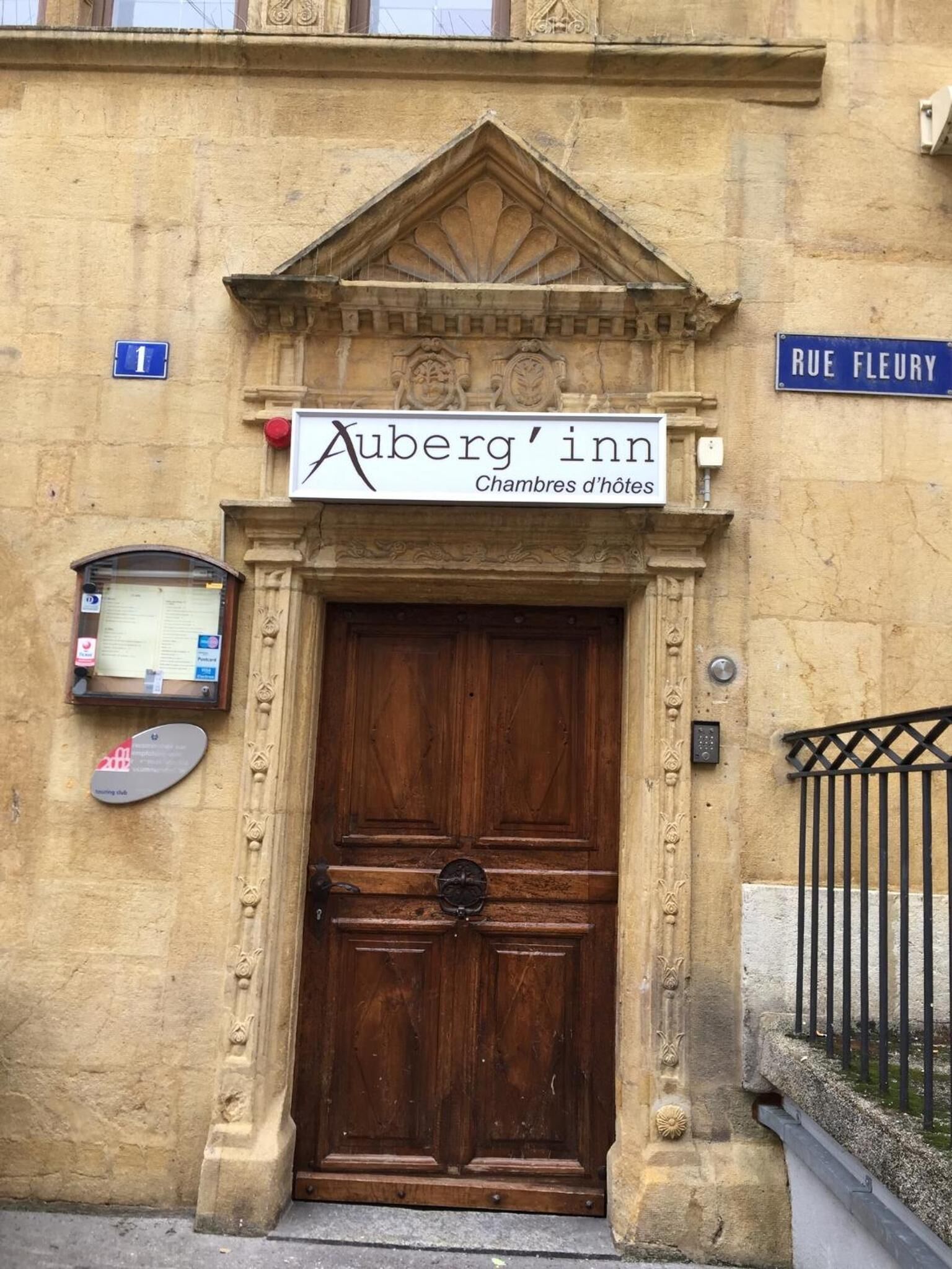 Un bâtiment doté d’une grande porte en bois, d’une enseigne indiquant « Auberge Auberg, chambres d’hôtes », et d’un panneau de rue indiquant « RUE FLEURY ».