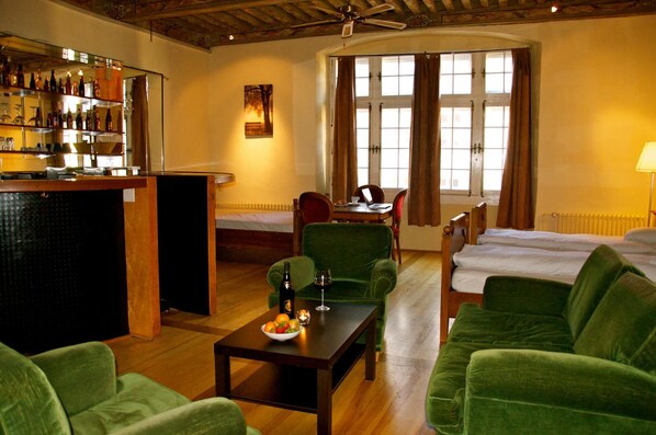 A hotel room with a bar area, a dining table with chairs, a green sofa, and a bed. - Aux chambres du Banneret (Neuchatel)