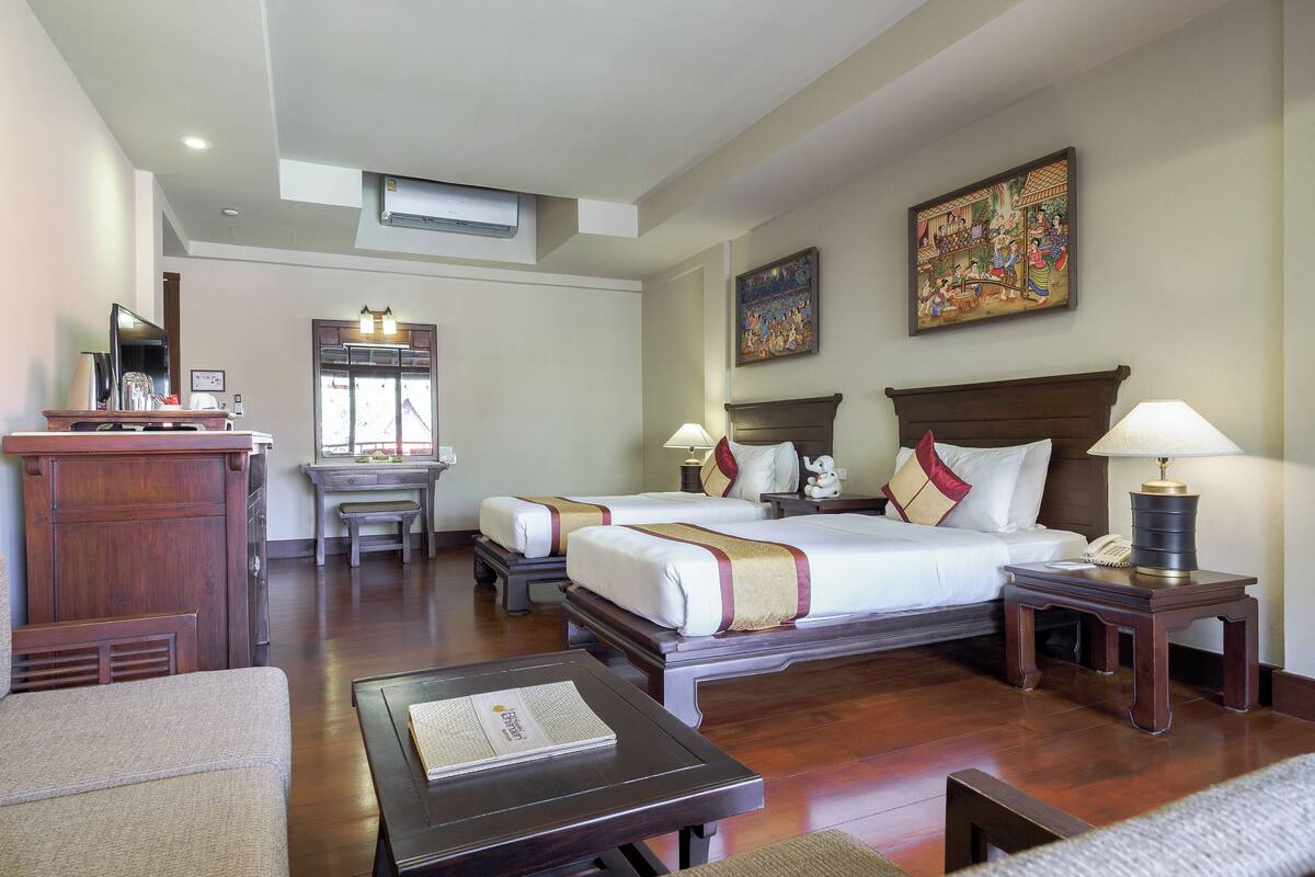 Une chambre d’hôtel avec deux lits, un bureau, une chaise, une lampe et des œuvres d’art accrochées aux murs.