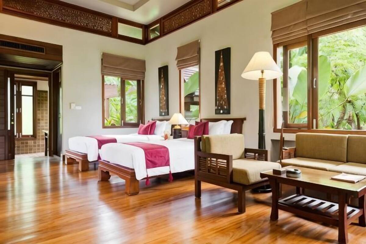 Une chambre d’hôtel avec deux lits, un canapé, une table basse et de grandes fenêtres avec des rideaux.
