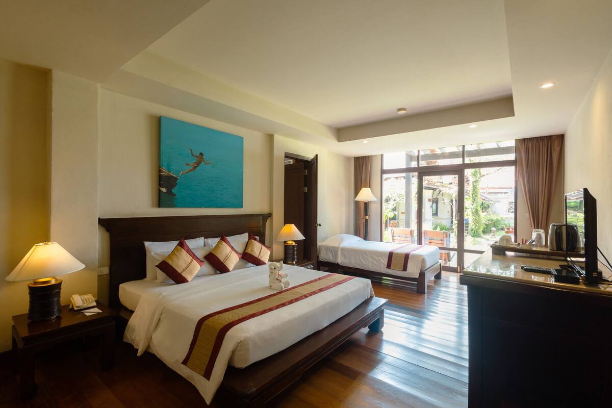 Une chambre d’hôtel avec un grand lit, un plus petit lit, un bureau avec une télévision et un tableau au mur.