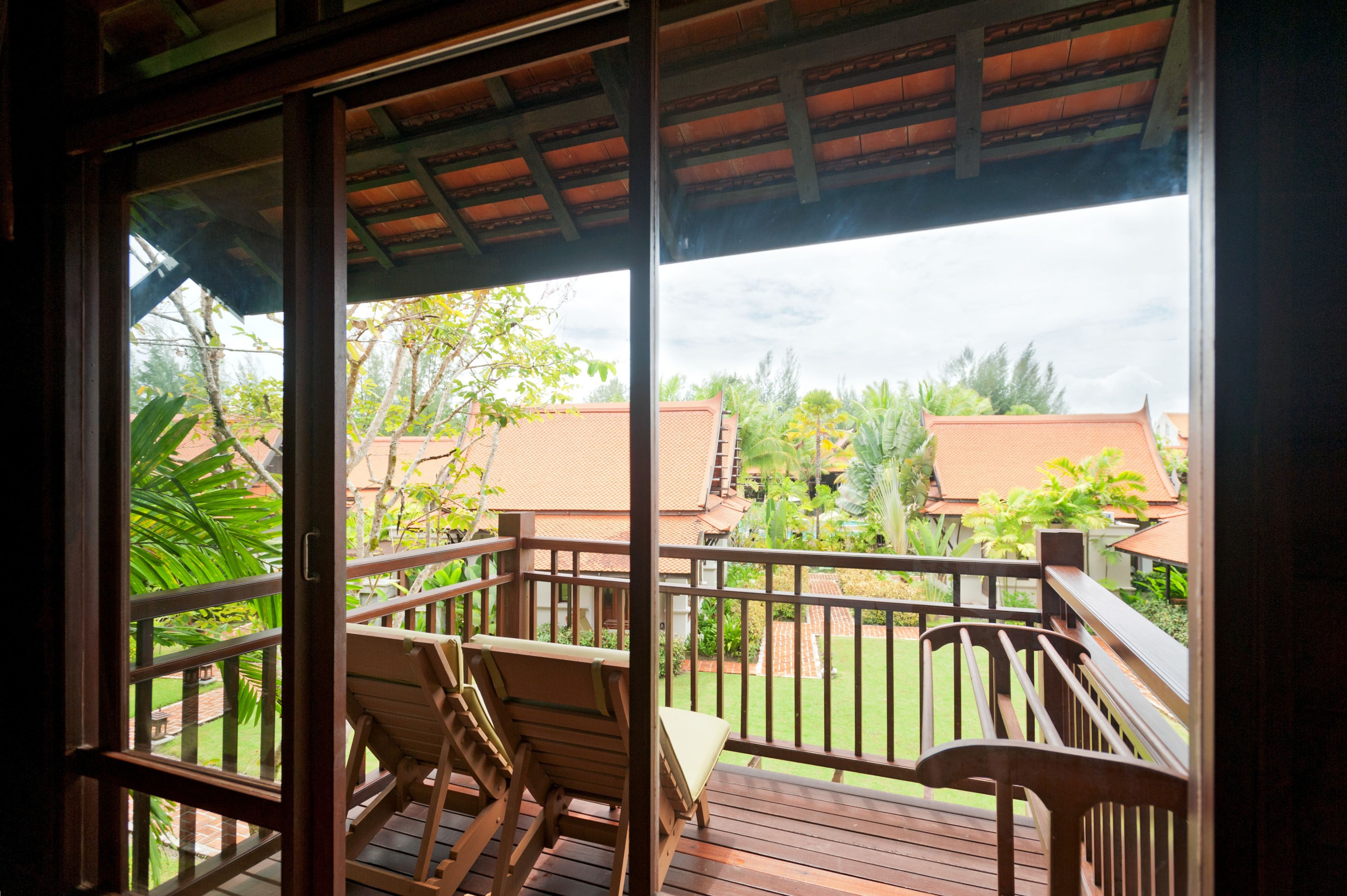 A wooden deck with a railing, two wooden chairs, and a view of a residential area with houses and greenery.