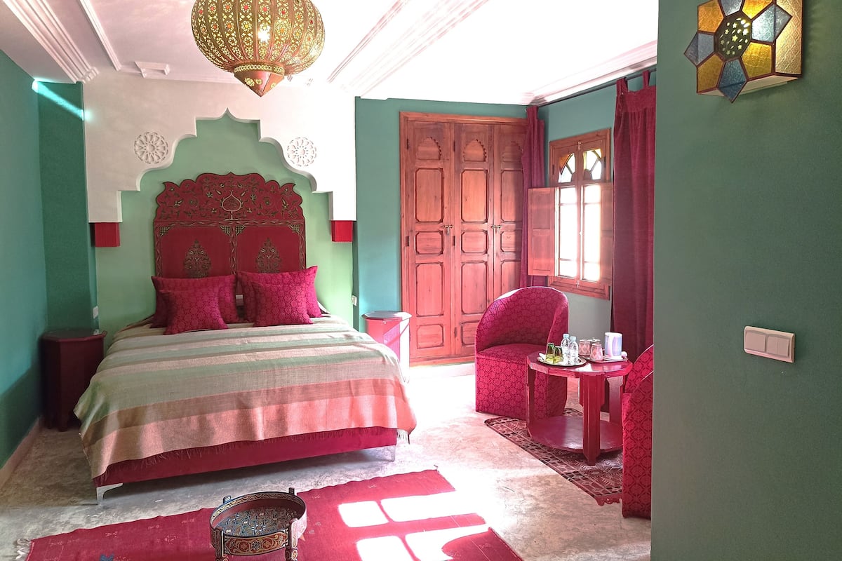 A bedroom with a bed, a chair, a table, and a decorative wall piece.