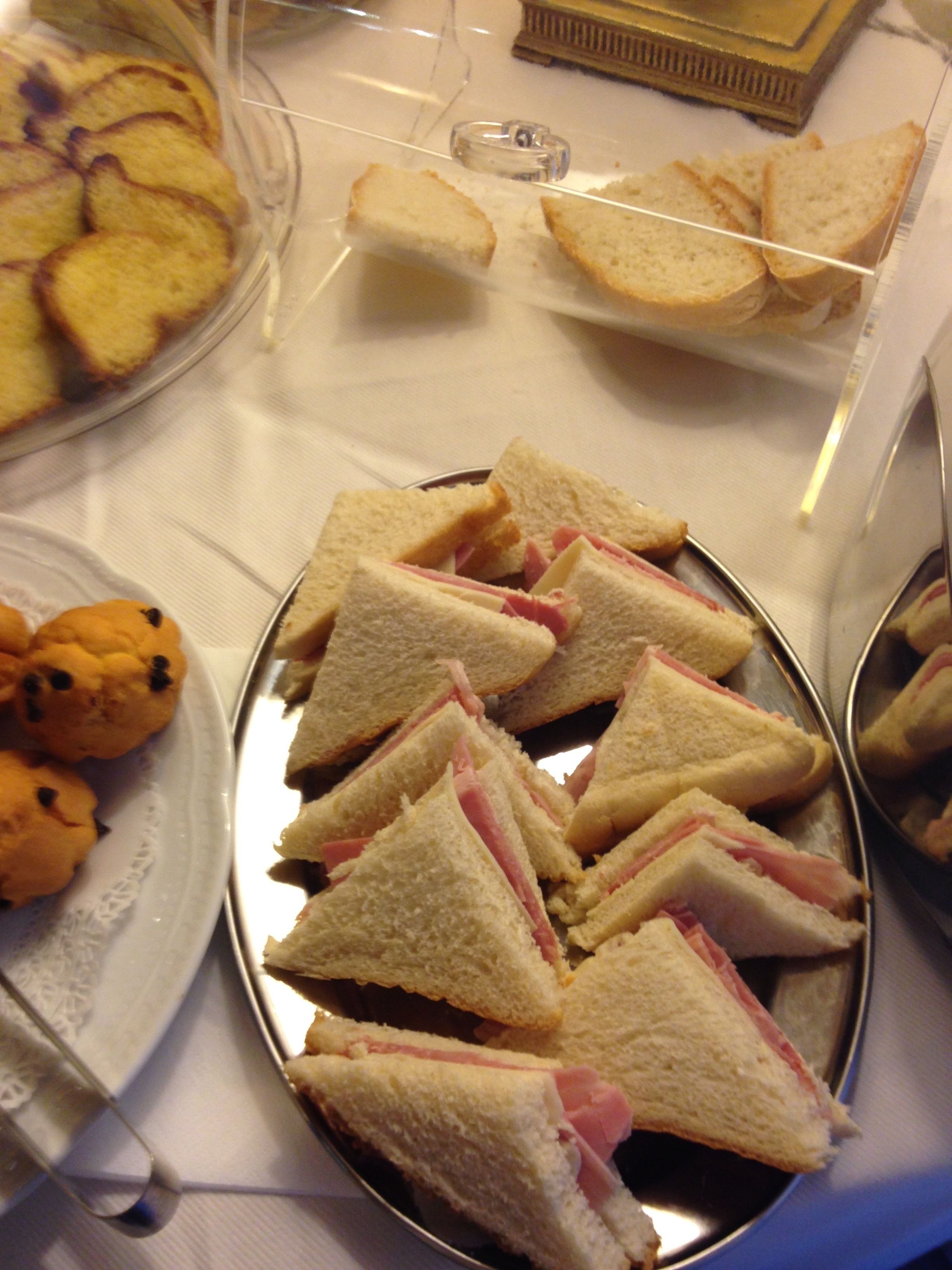 A tray of ham and cheese sandwiches, a plate of cookies, and a container of bread slices.