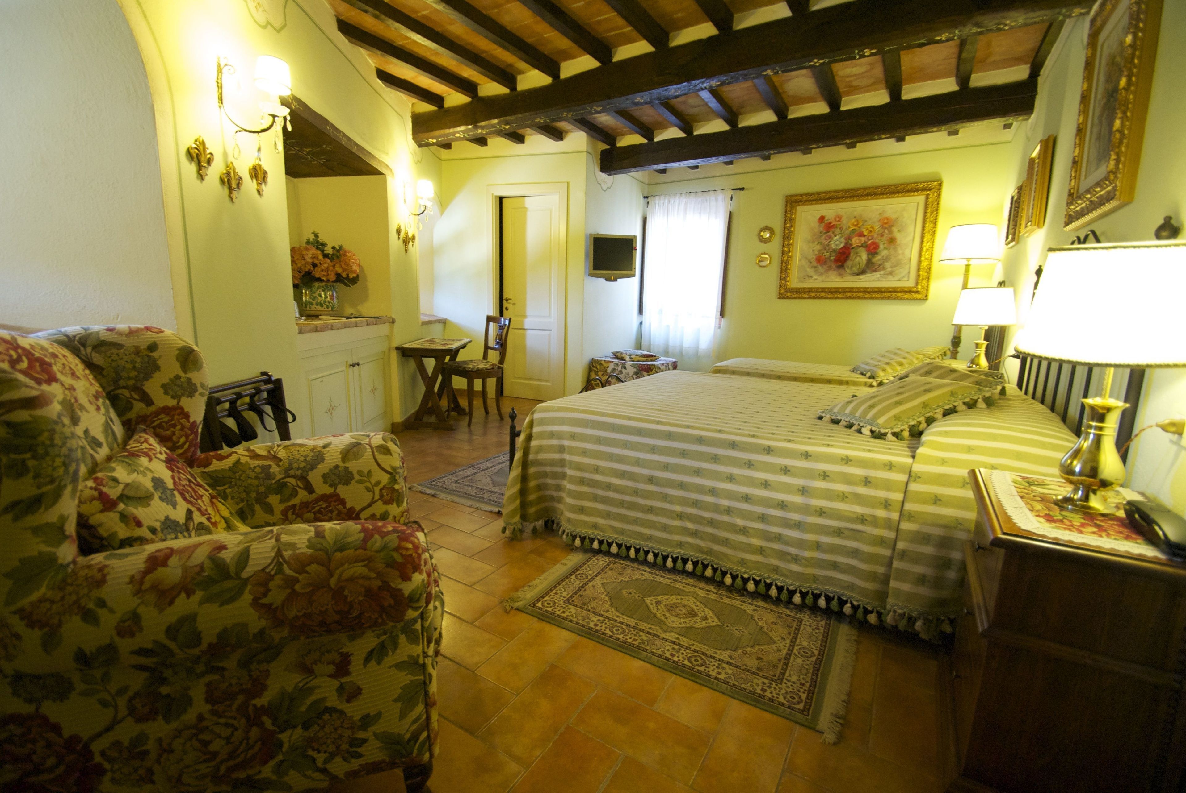 A bedroom with a bed, a chair, a small table, a TV, and a lamp.