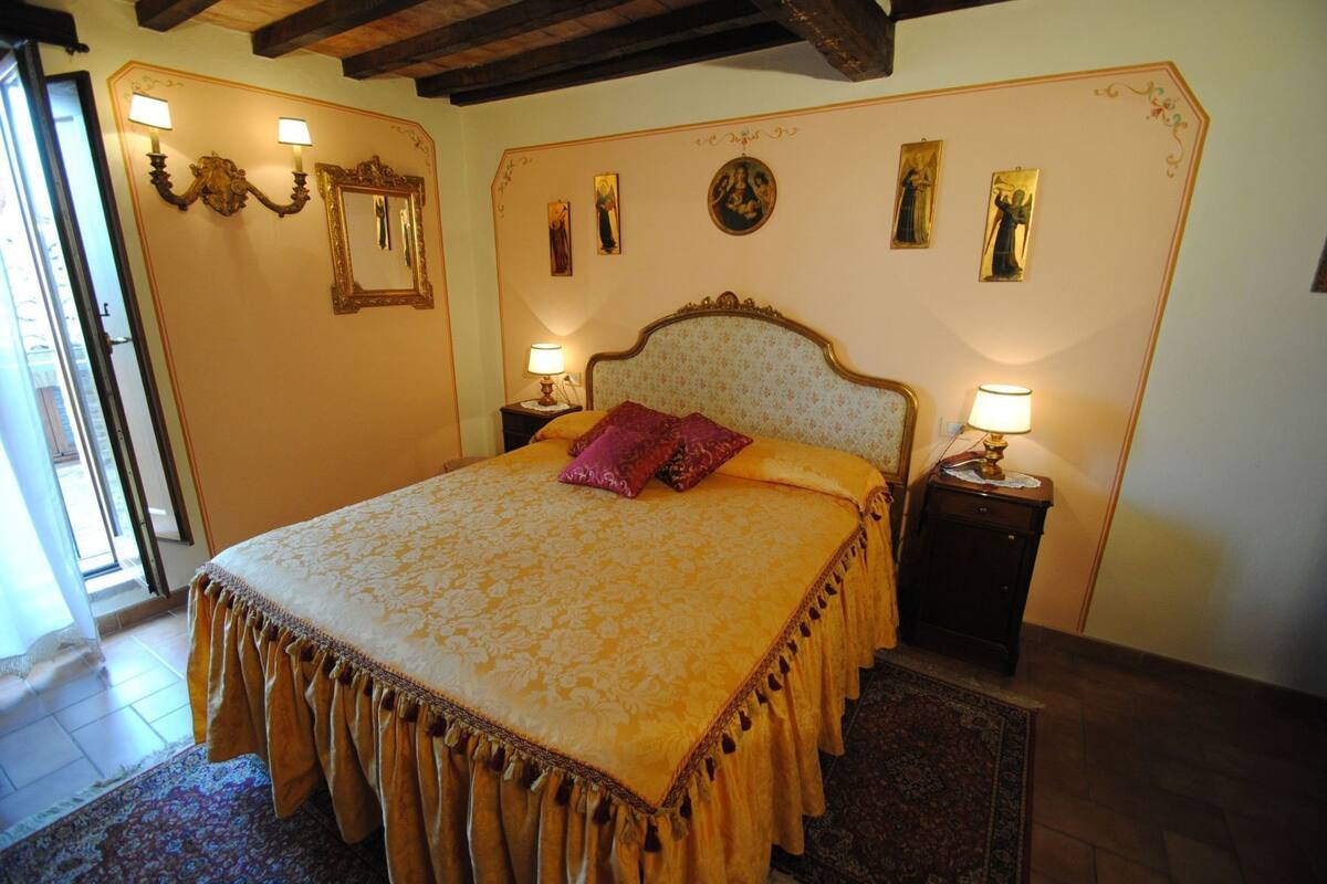 A bedroom with a large bed, two bedside tables, a mirror, wall-mounted lamps, and religious artwork.