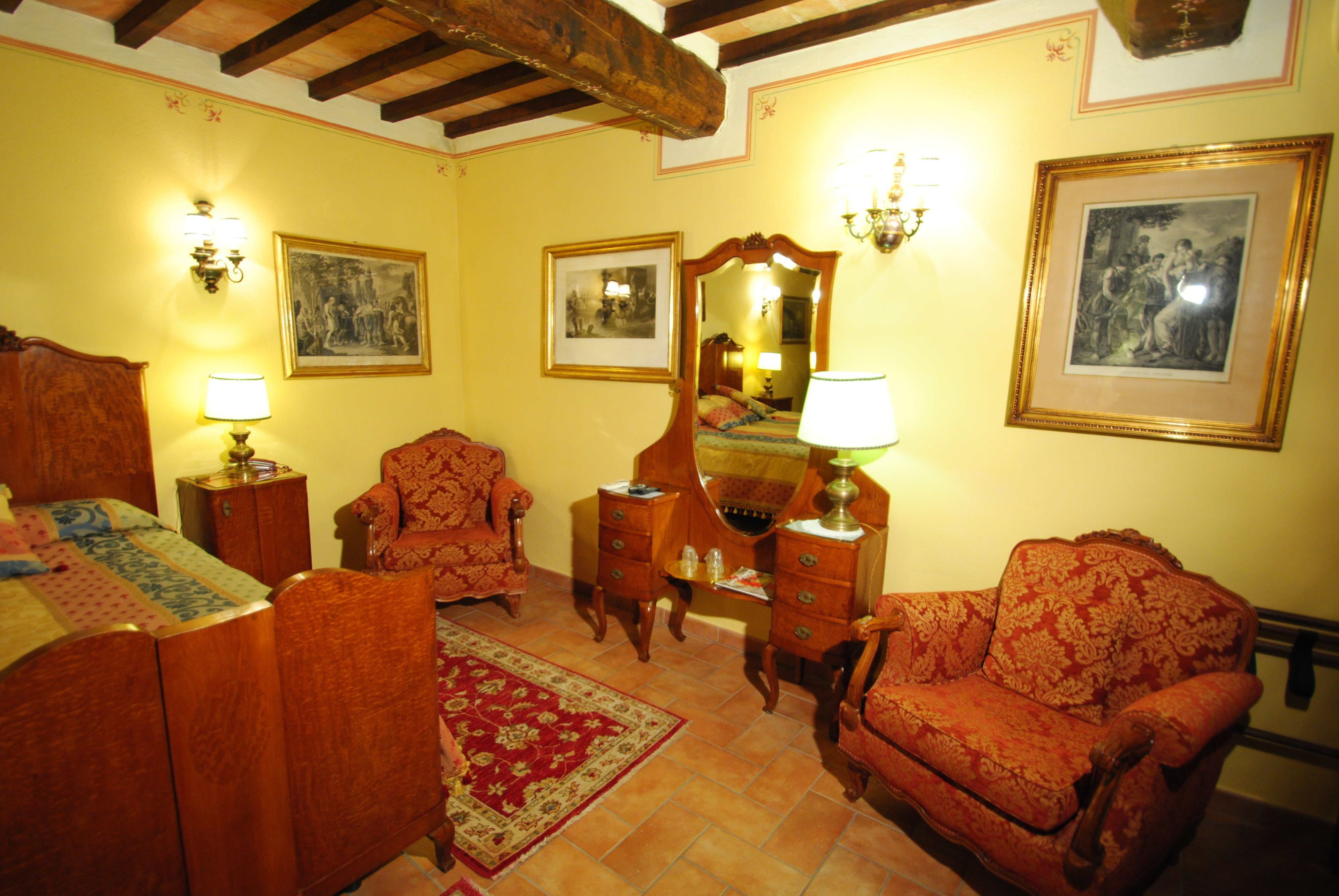 A traditional room with a bed, two armchairs, a wooden dresser, and a mirror.